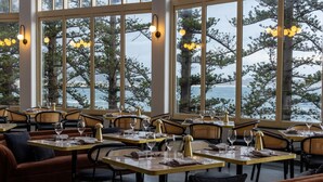 A restaurant with tables set for dining, large windows with a view of trees and water, and warm lighting. - Crowne Plaza Terrigal Pacific by IHG (Terrigal)