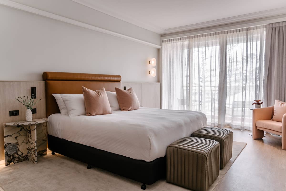 Un dormitorio moderno con una cama grande, una mesita de noche, un área de descanso y una ventana con cortinas de gasa.