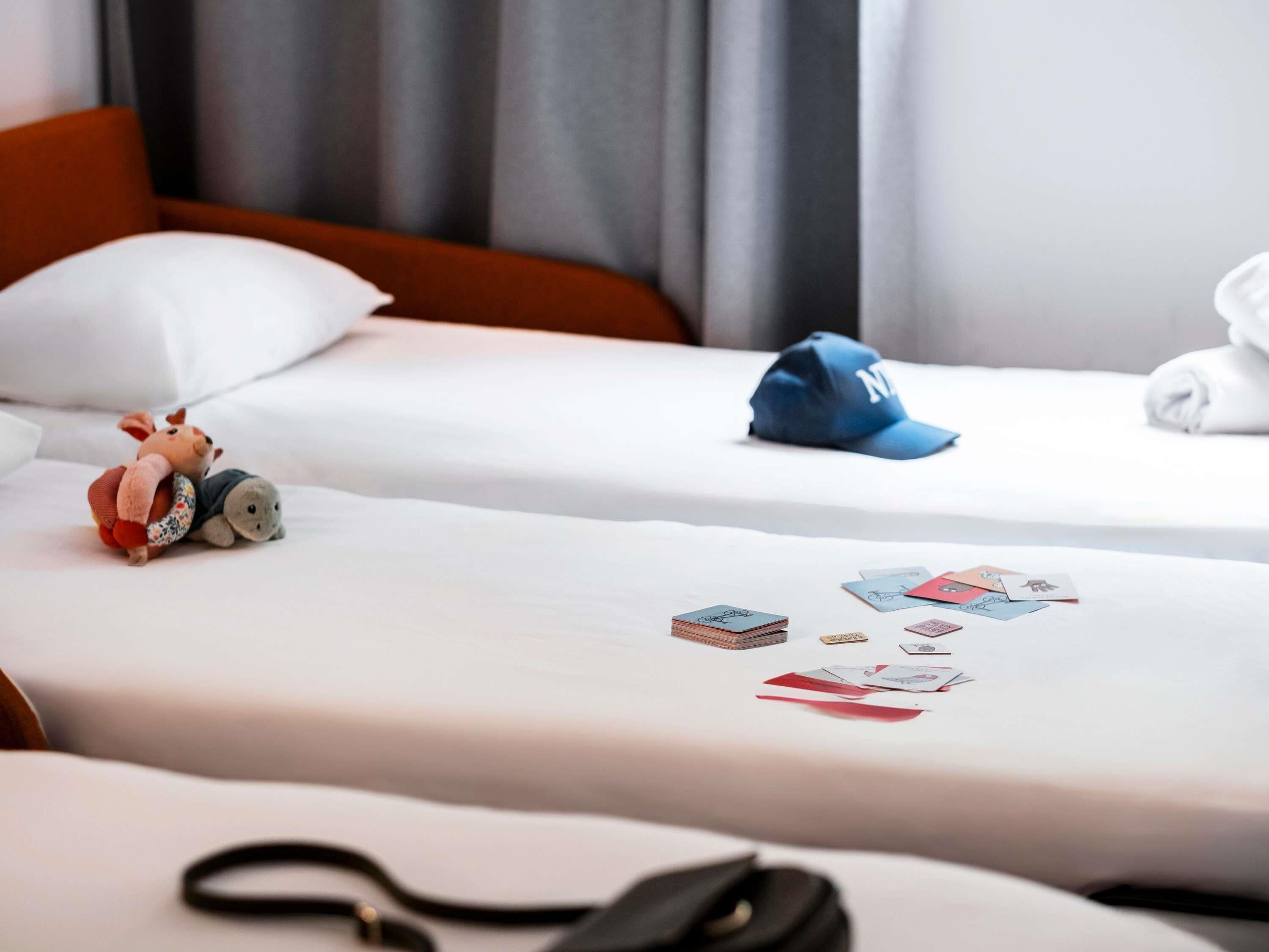 Two beds with white linens, a plush toy, a cap, and playing cards on the beds.