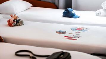 Two beds with white linens, a plush toy, a cap, and playing cards on the beds.