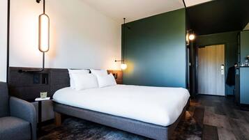 A modern hotel room with a large bed, a nightstand, a bedside table, and a wall-mounted lamp.