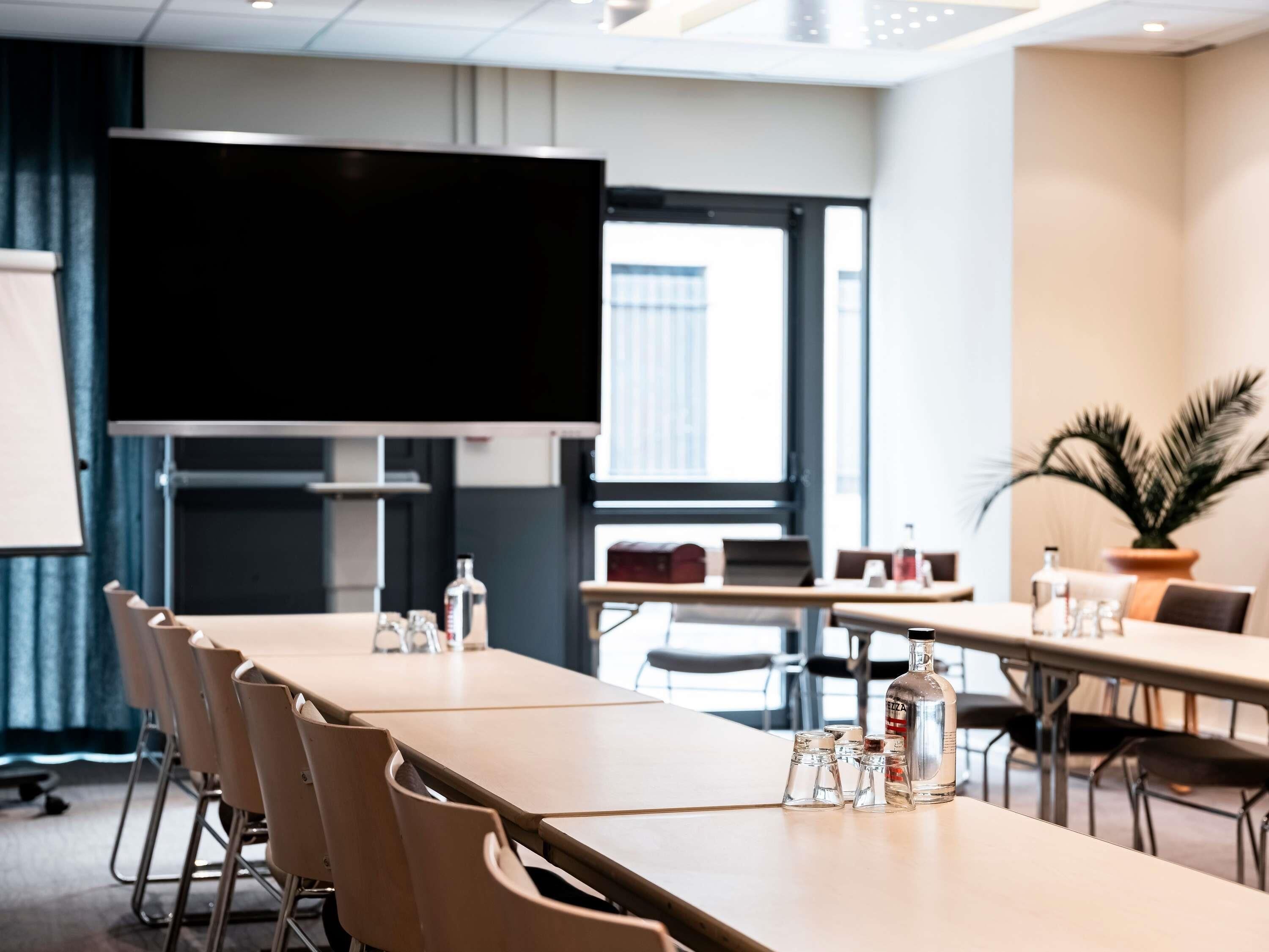 A conference room with a long table, chairs, a television, and a potted plant.
