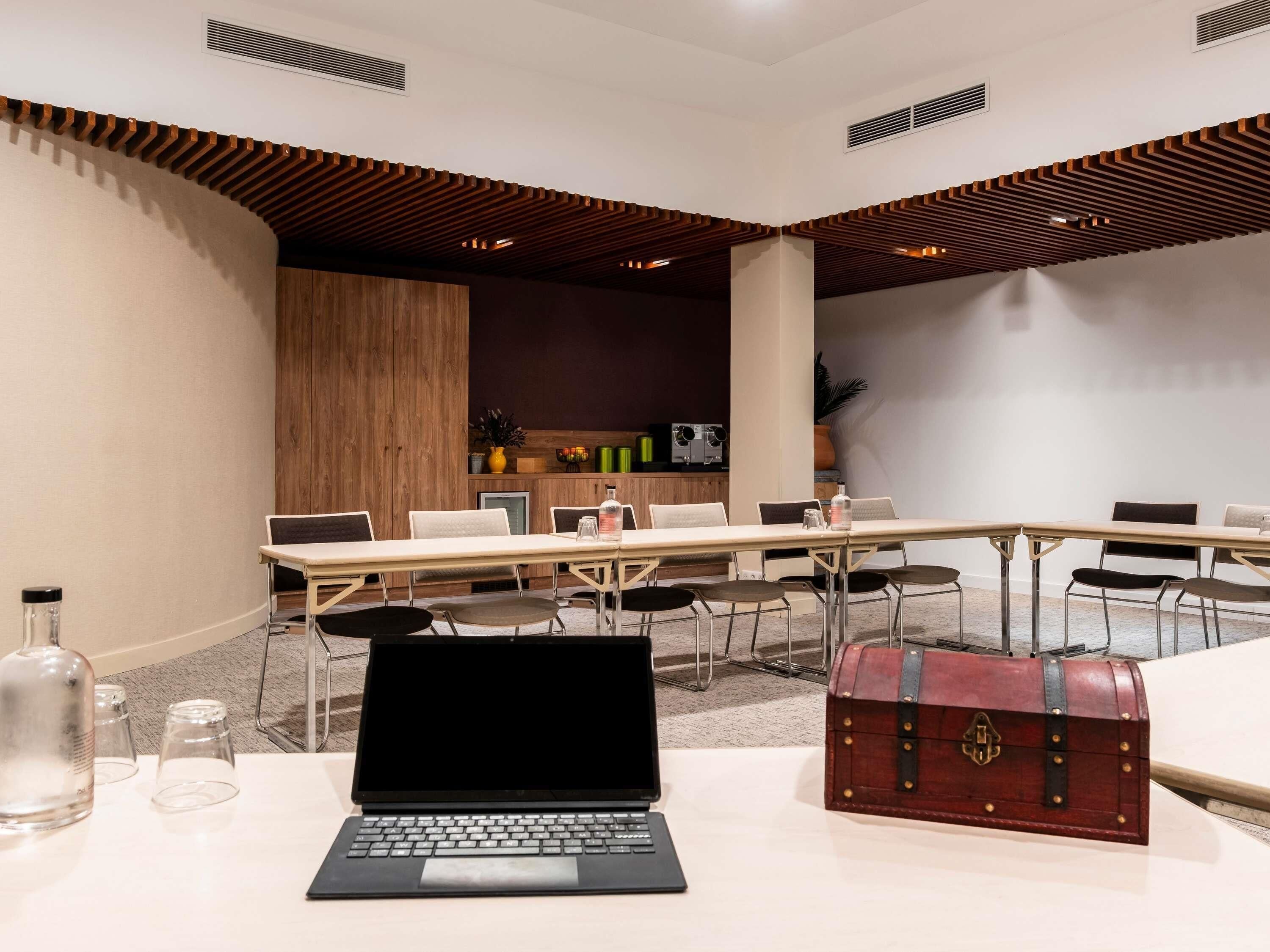 A conference room with a long table, chairs, a laptop, a red leather briefcase, and a wooden accent wall.