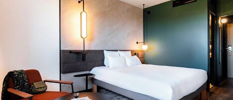 Una habitación de hotel moderna con una cama grande, una mesita redonda pequeña, una silla y un sofá.
