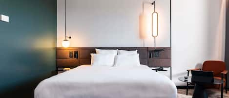 A modern hotel room with a large bed, bedside tables, a desk, and a chair.