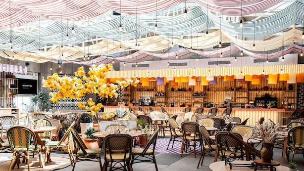 A spacious indoor area with wicker chairs and tables, a bar area with shelves of bottles, and a large floral arrangement. - Novotel Atria Nimes Centre (Nîmes)
