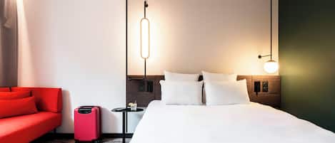 Et hotelværelse med en seng, en rød sofa, et lille bord og en kuffert.