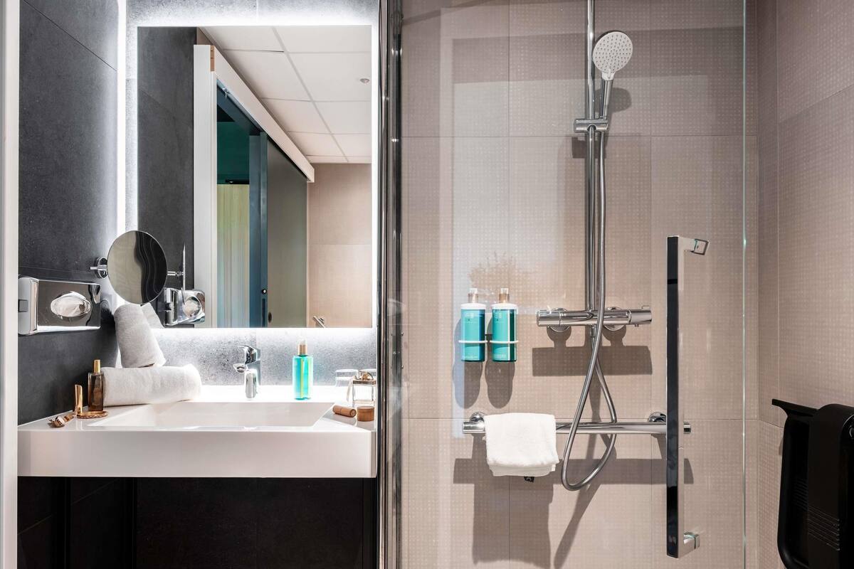 A modern bathroom with a glass shower enclosure, a sink with a mirror, and toiletries on the counter.