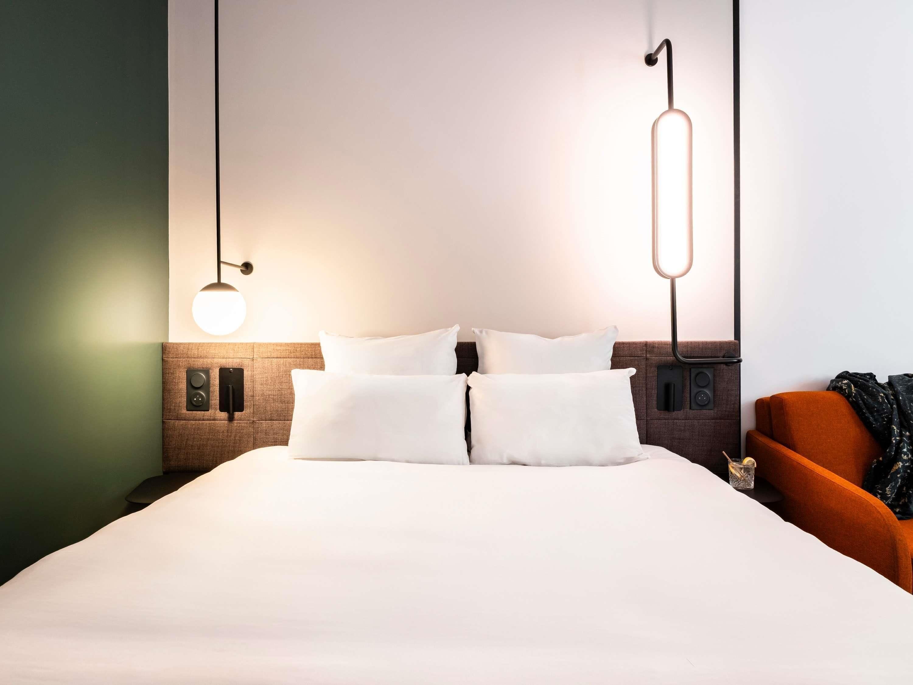 A hotel room with a large bed, two bedside tables, a wall-mounted light fixture, and a chair.