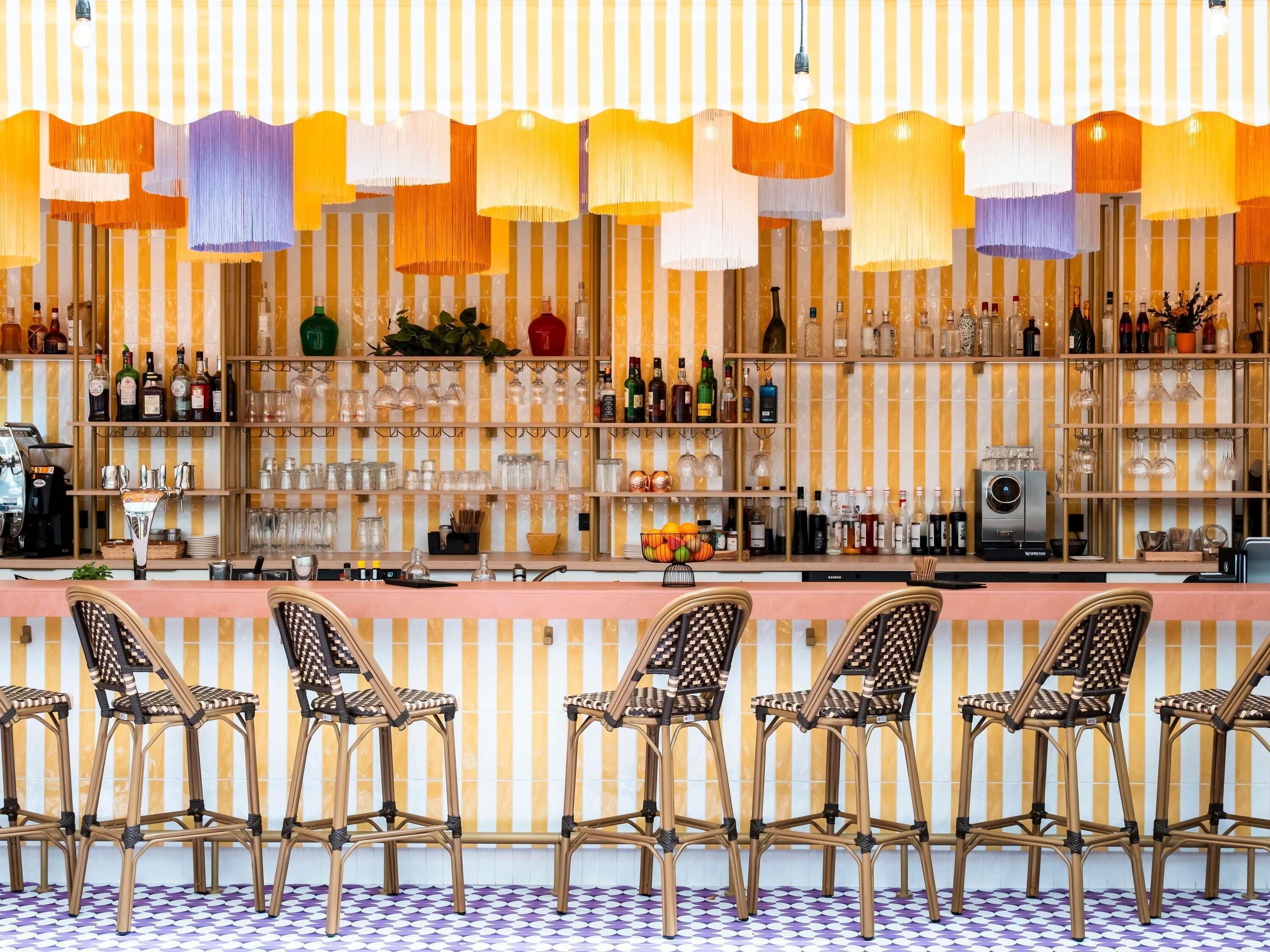 A bar area with wicker chairs, shelves of bottles and glasses, and a patterned floor.