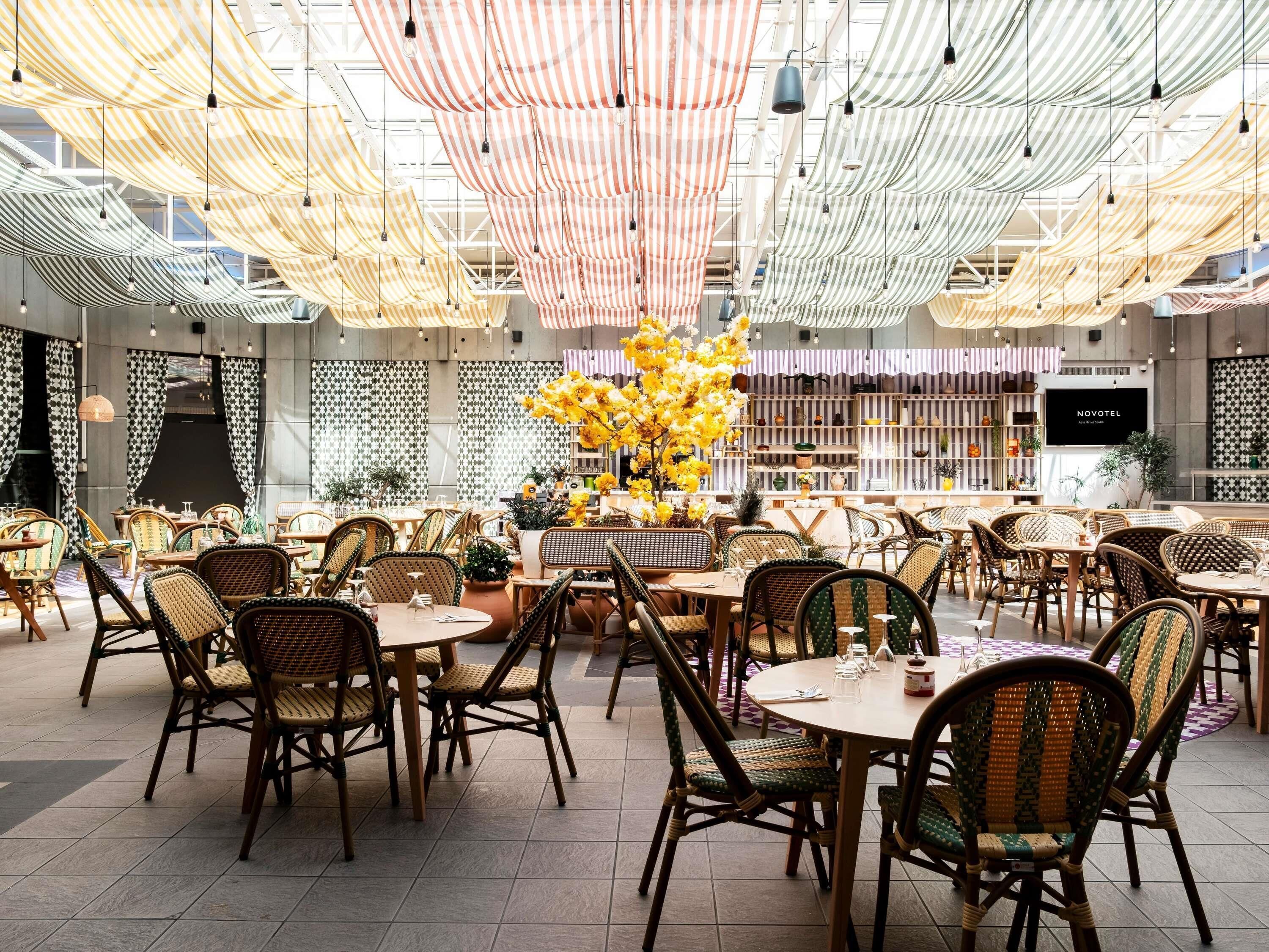 A restaurant with round tables, wicker chairs, and hanging fabric ceilings.