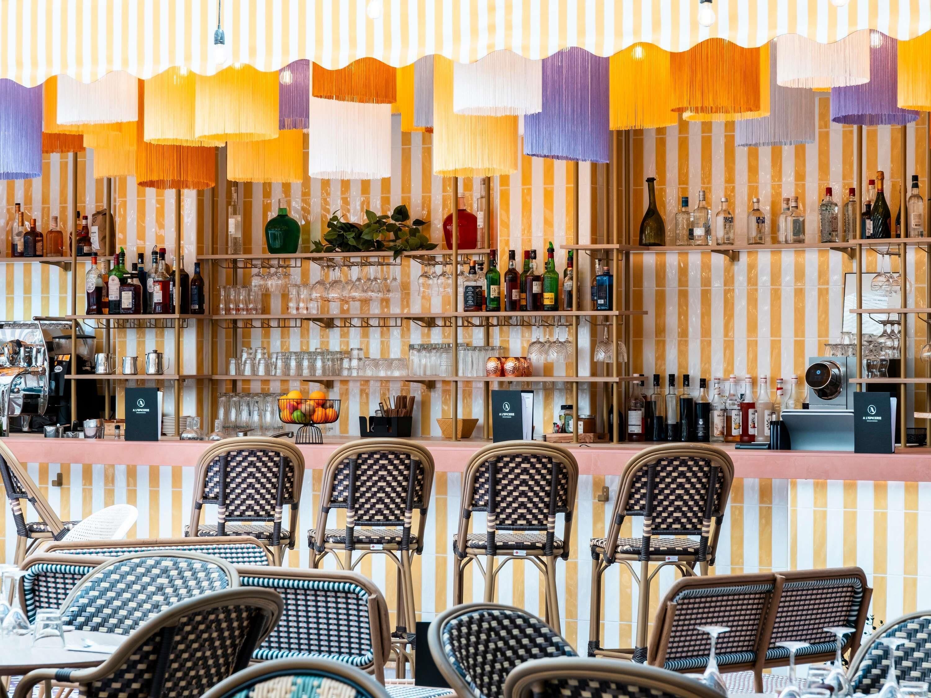 A bar area with wicker chairs, shelves of bottles, glasses, and a striped wall.