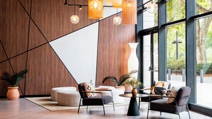 A modern lobby with a geometric wall design, comfortable seating, and large windows offering a view of the outdoors. - Novotel Atria Nimes Centre (Nîmes)