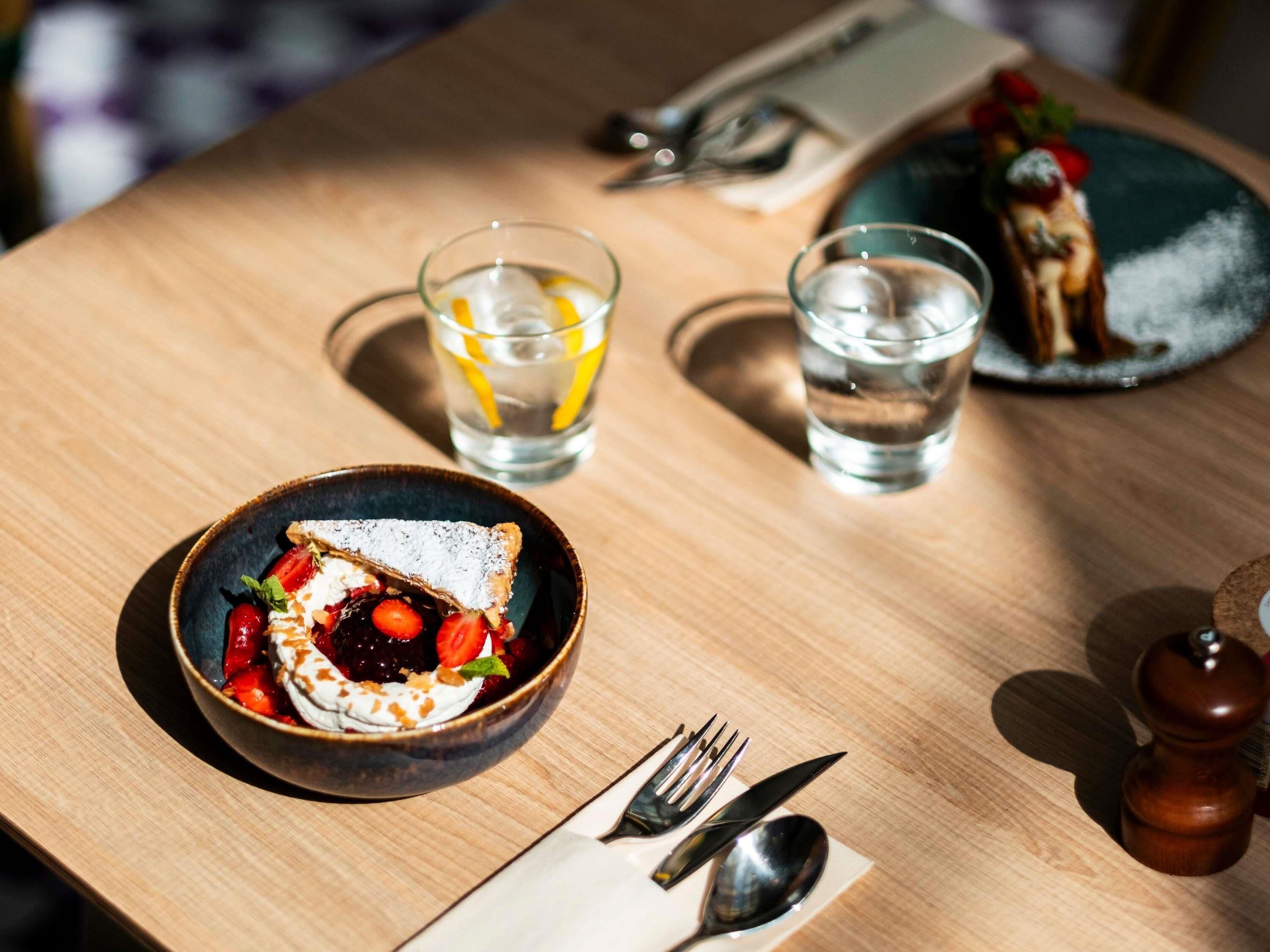 A table with a dessert bowl, two glasses of water, cutlery, and a plate with a dessert.
