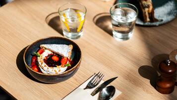 A table with a dessert bowl, two glasses of water, cutlery, and a plate with a dessert.