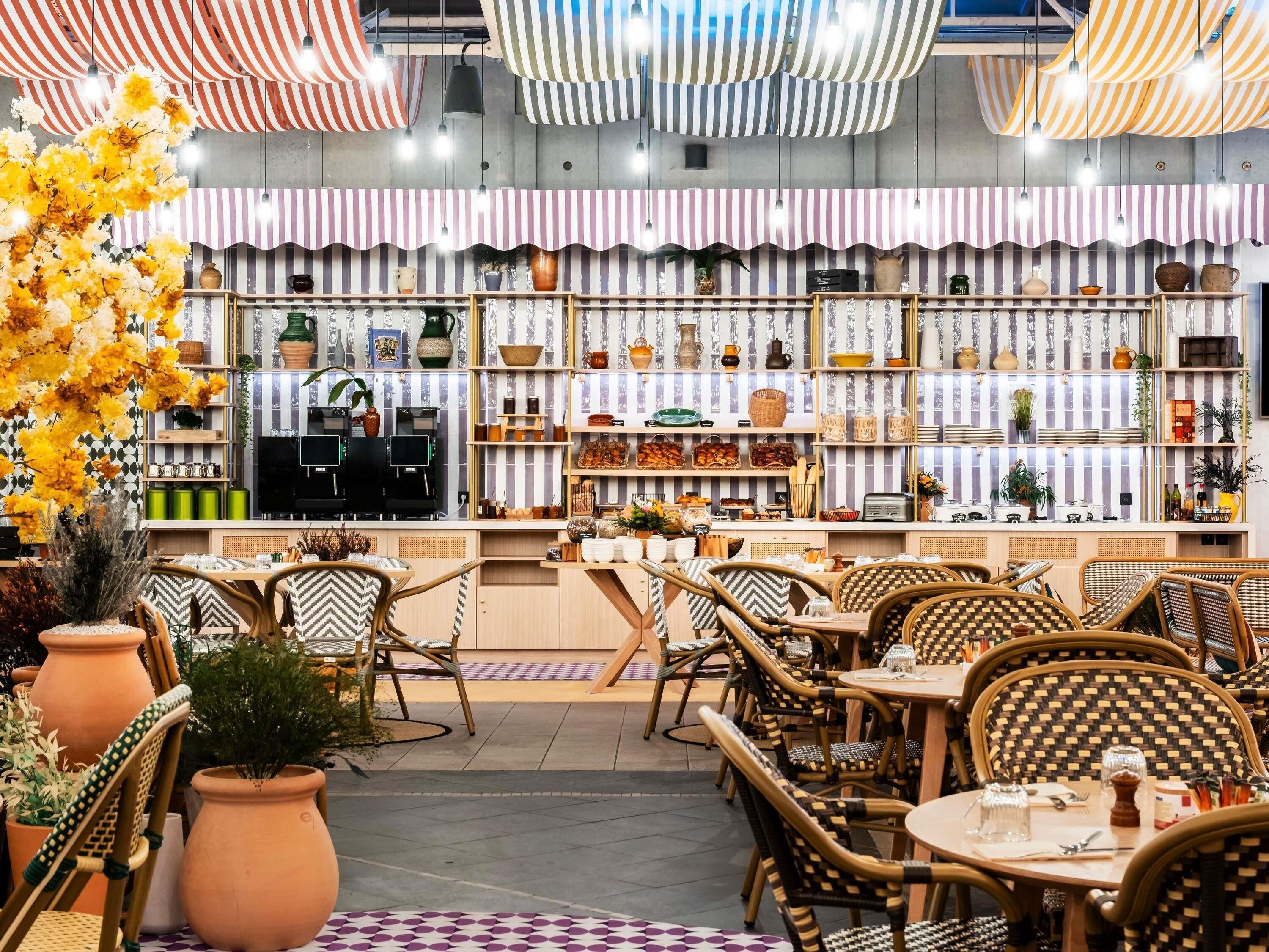 A restaurant with striped ceiling decorations, wicker furniture, and shelves with various items.
