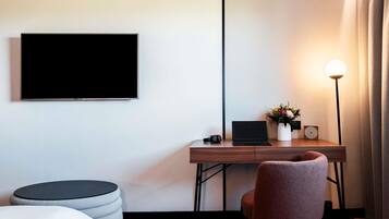A modern hotel room with a flat-screen TV, a desk with a laptop, a lamp, and a chair.