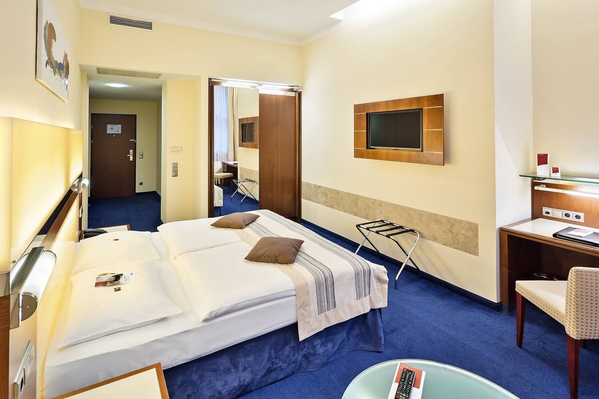 A hotel room with a bed, a desk, a chair, a TV, and a mirror.