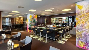 Zona de bar moderna con una barra larga, varios taburetes y una amplia variedad de botellas. También hay varias mesas con sillas para comer.