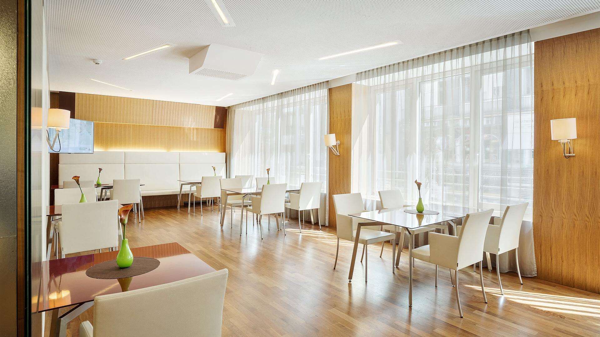 A modern hotel lobby with a spacious seating area, wooden panel walls, and large windows with sheer curtains.