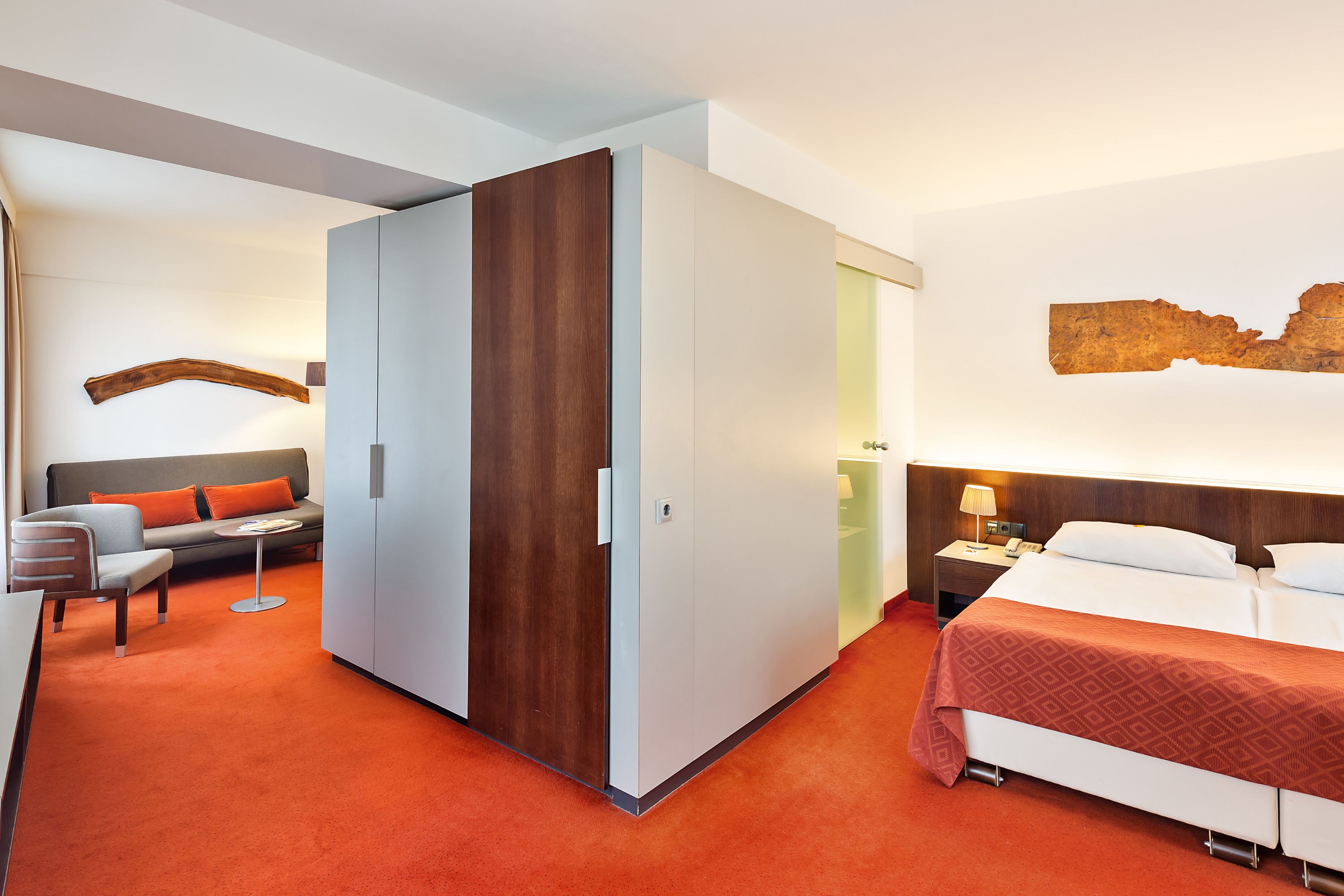 A modern hotel room with a bed, a sofa, a desk, and a wardrobe.