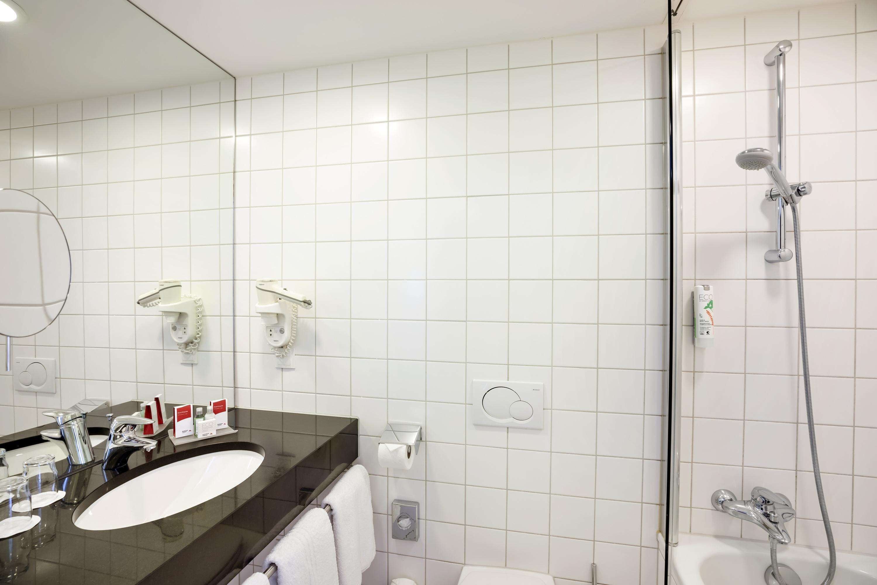 Ein modernes Badezimmer mit einem großen Spiegel, einem Waschbecken, einer Dusche und einer Toilette.