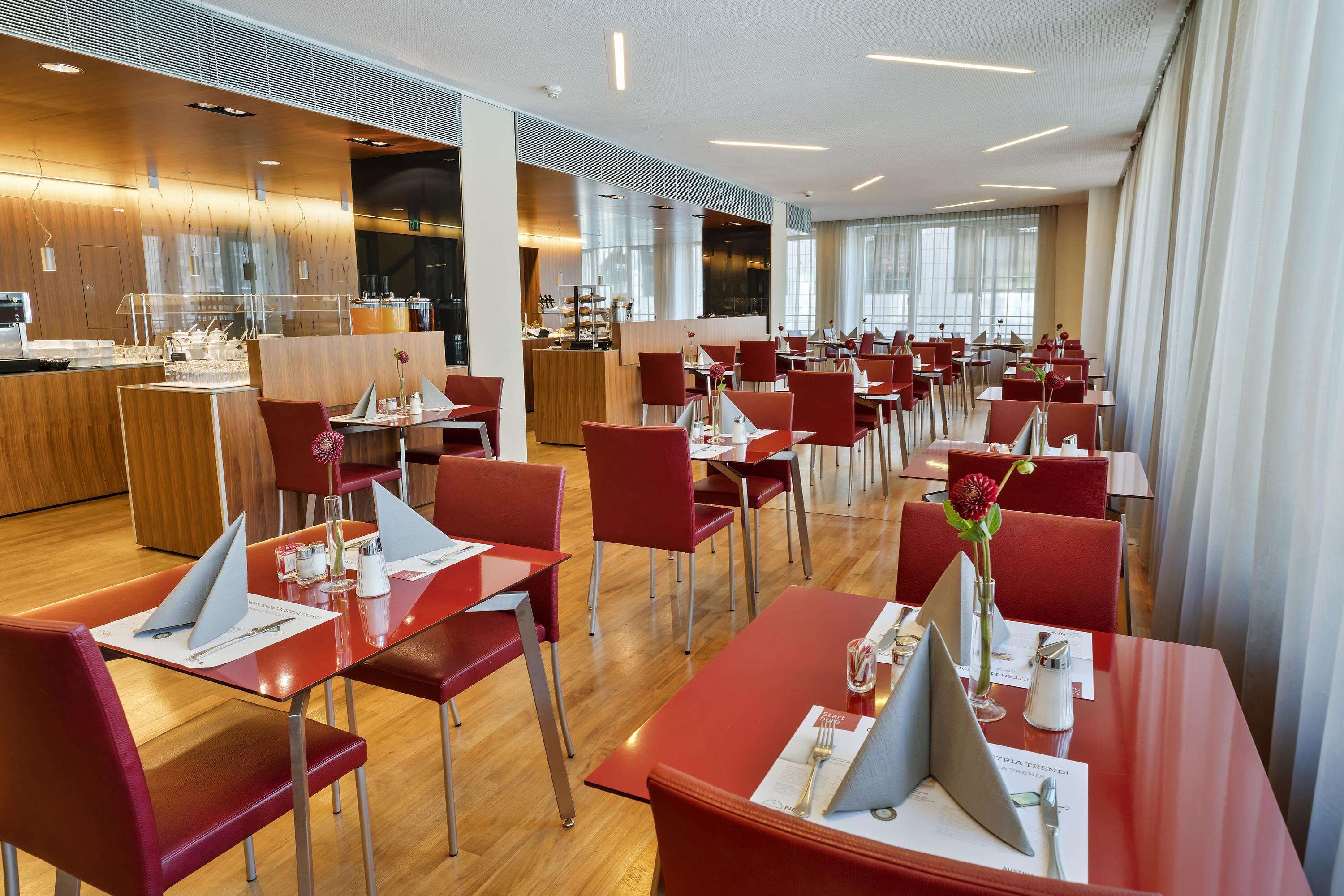 A modern restaurant with red chairs and tables, a wooden counter, and large windows.