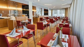 A modern restaurant with red chairs and tables, a wooden counter, and large windows.