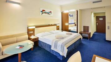 Quarto de hotel com uma cama, um sofá, uma mesinha e um espelho.
