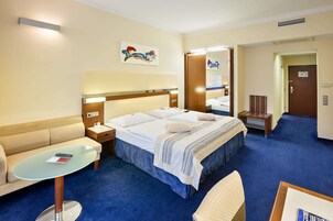 Quarto de hotel com uma cama, um sofá, uma mesinha e um espelho.