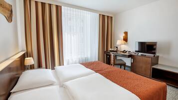 Quarto de hotel com cama, escrivaninha e televisão, além de uma luminária.
