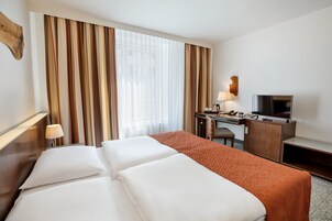 Quarto de hotel com cama, escrivaninha e televisão, além de uma luminária.