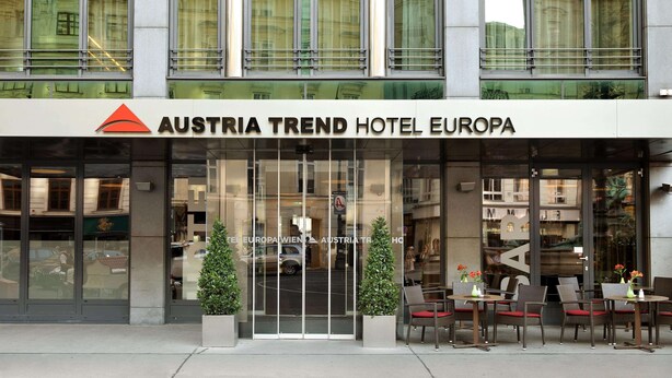 Exterior del Austria Trend Hotel Europa con fachada de vidrio, zona de estar al aire libre y vista despejada a la calle.