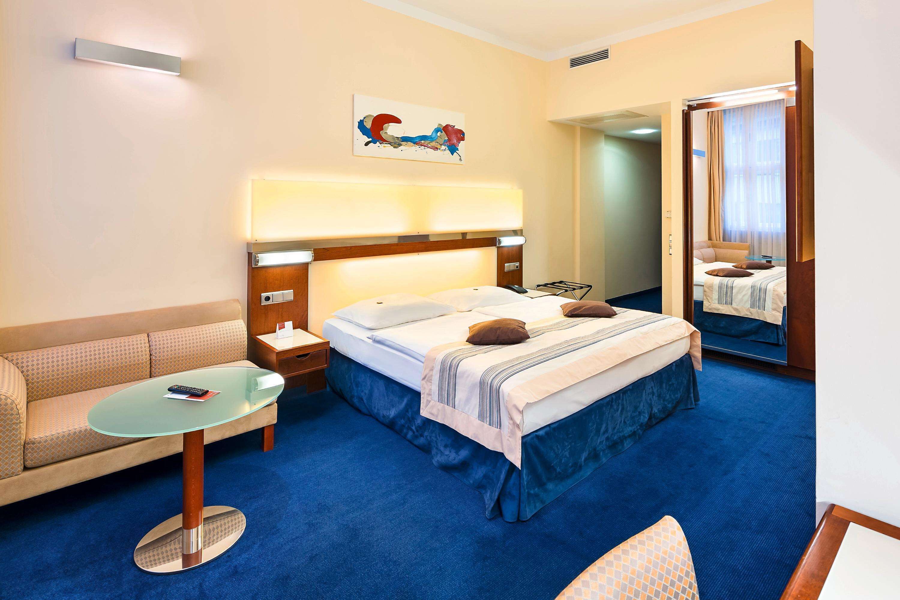 Una habitación de hotel con cama, sofá, una mesita y un espejo.