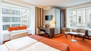 Habitación de hotel con cama, escritorio, sillas, televisor y vista de la ciudad.
