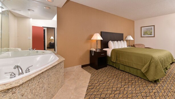 A hotel room with a large bathtub, a bed with green bedding, a nightstand with lamps, and a framed picture on the wall. - Quality Inn & Suites Matteson near I-57 (Matteson)