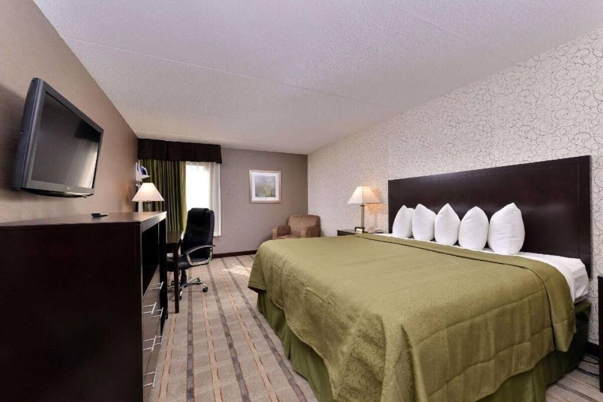 Quarto de hotel com uma cama, uma escrivaninha, uma televisão e uma cadeira.