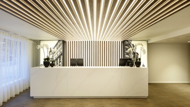 Un comptoir d’accueil moderne, doté d’un plateau en marbre blanc, flanqué de deux écrans d’ordinateur, et surmonté d’un panneau lumineux vertical.
