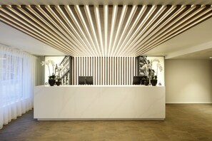 Un comptoir d’accueil moderne, doté d’un plateau en marbre blanc, flanqué de deux écrans d’ordinateur, et surmonté d’un panneau lumineux vertical.