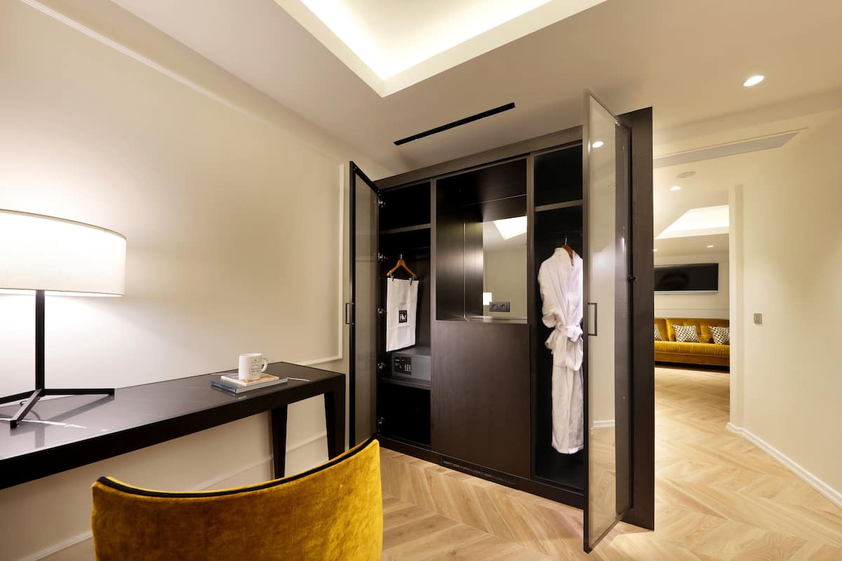 A hotel room with a desk, a chair, a robe hanging on the door, and a bed in the background.