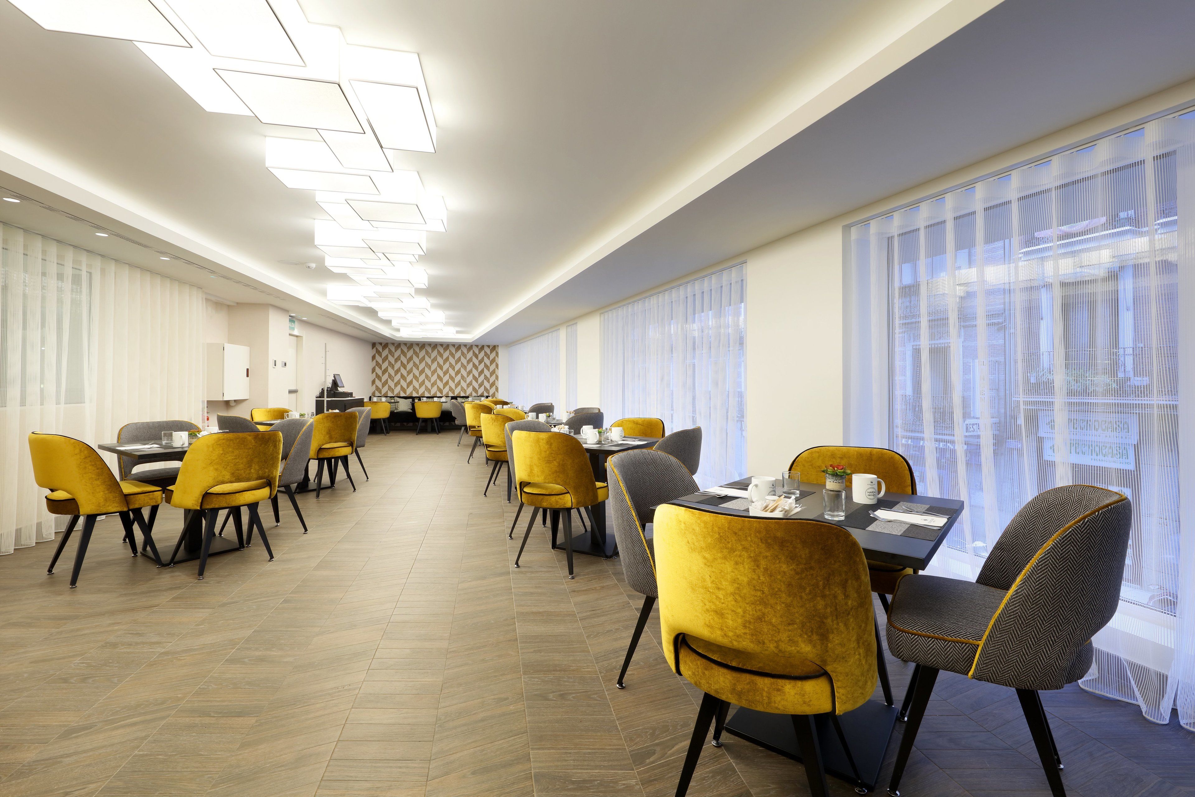 A modern dining area with yellow and grey chairs, a long table, and a patterned wall.