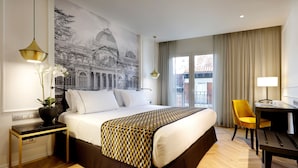 Une chambre d’hôtel avec un grand lit, un bureau, une chaise, une plante en pot et une fresque murale.