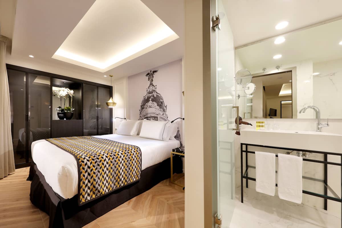 A modern hotel room with a large bed, a bathroom with a large mirror, and a decorative wall piece.