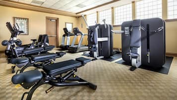 Un gimnasio con diversos equipos de ejercicio, incluyendo cintas de correr, elípticas y bancos de pesas.