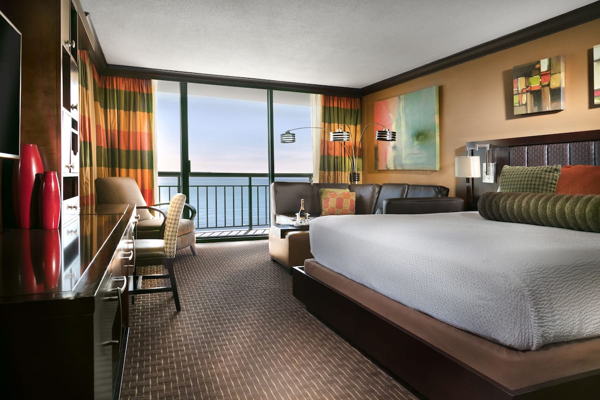 A hotel room with a large bed, a desk, a chair, and a view of the ocean.