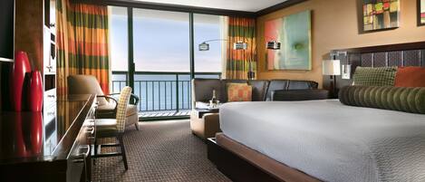 Ein Hotelzimmer mit einem großen Bett, einem Schreibtisch, einem Sessel und Blick aufs Meer.