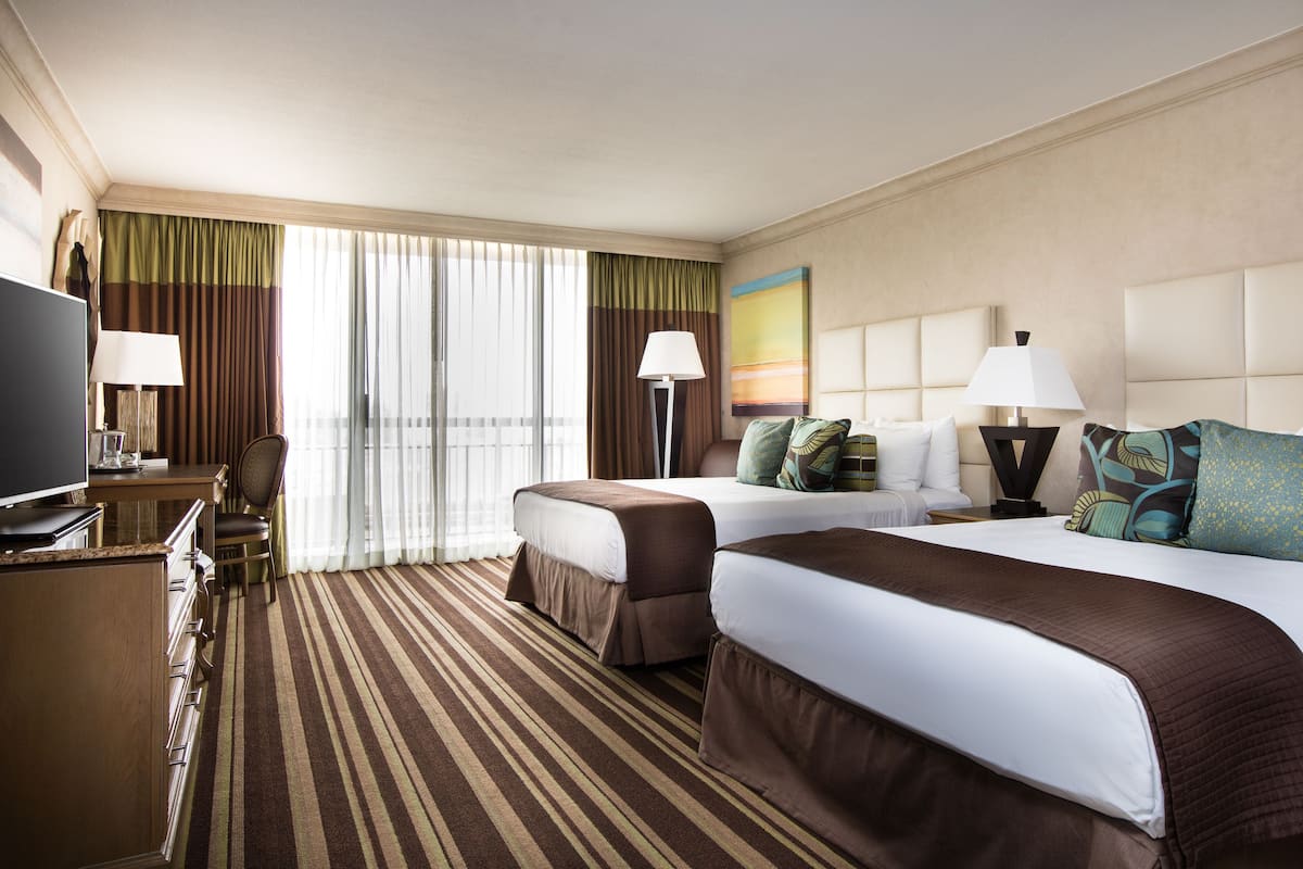 A hotel room with two beds, a TV, a desk, and a lamp.