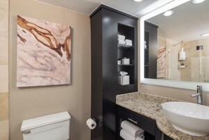 A modern bathroom with a marble wall, a black cabinet with shelves, a sink, and a toilet.