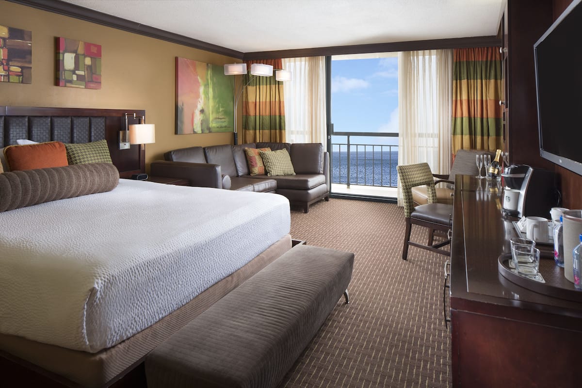 A hotel room with a large bed, a sofa, a desk with a chair, and a TV.