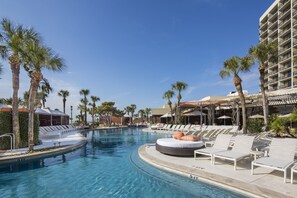 A pool area with lounge chairs and palm trees, surrounded by a building with balconies. - The San Luis Resort, Spa & Conference Center (Galveston)